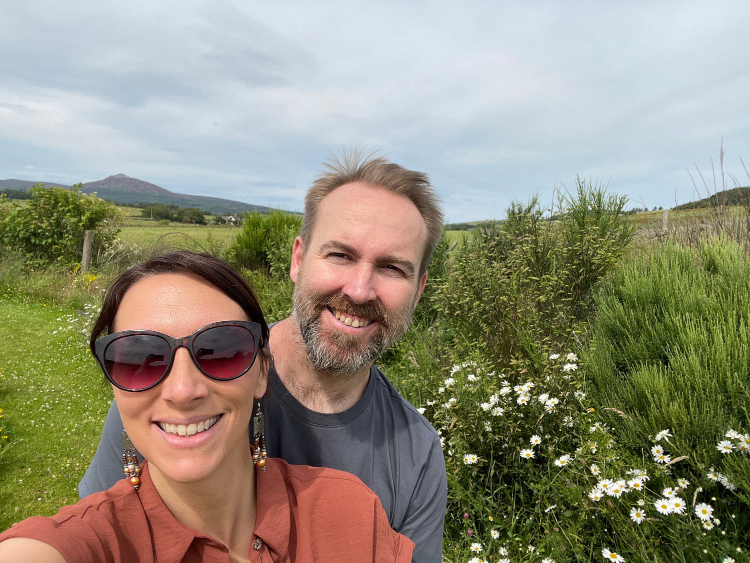 Hayley And Al taking a selfie in a field with greenery and flowers.