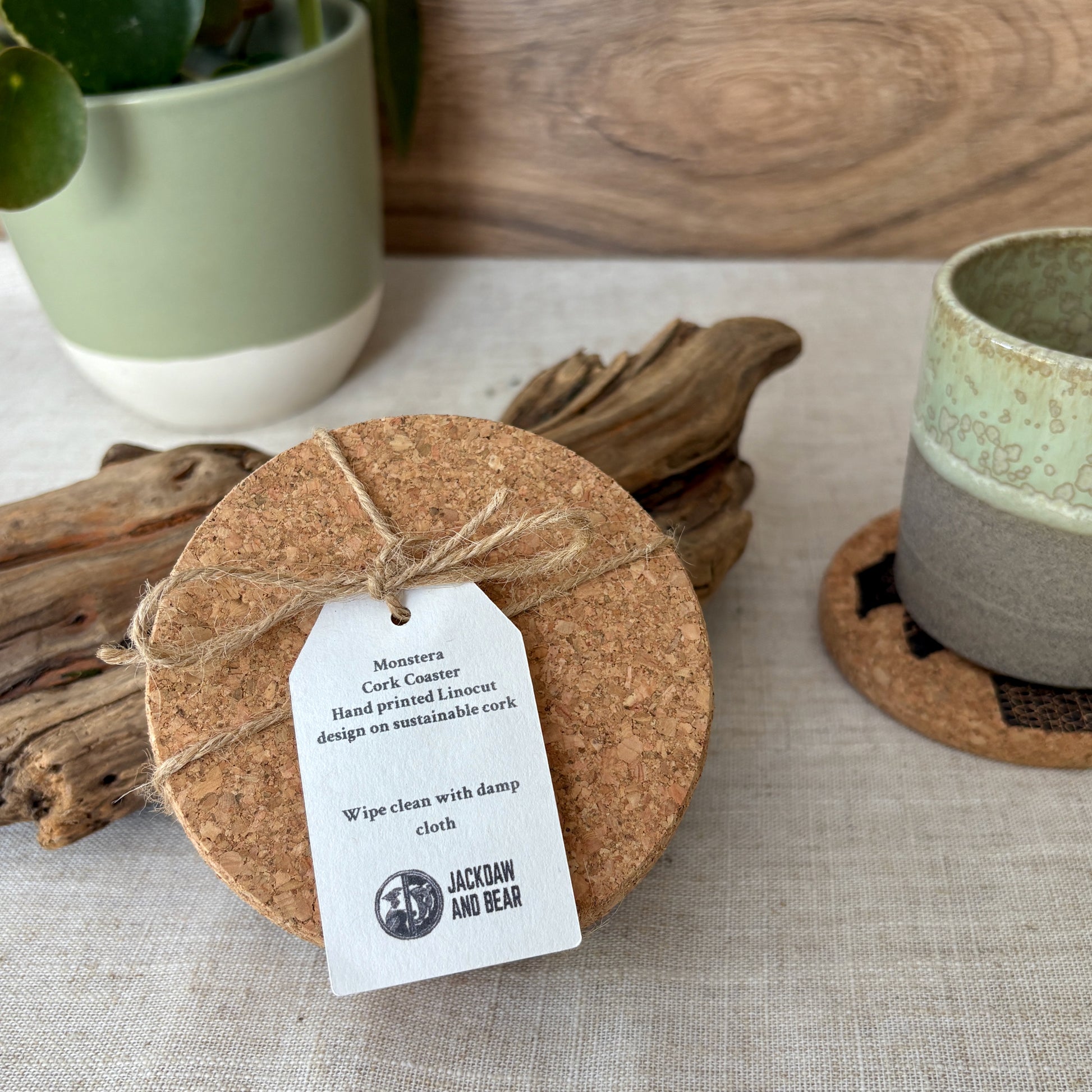 Cork coaster with a tag on a textured surface with a plant and wooden elements in the background