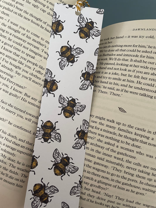 Bumblebee bookmark with white background and mini bees scattered across the bookmark. bookmark lays on paperback book