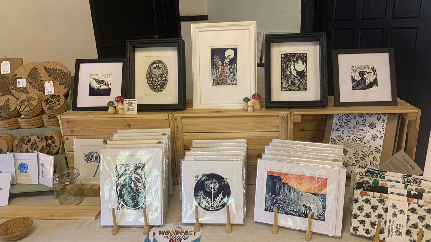 Jackdaw And Bear Stall at Chilham Craft Fair showing framed and mounted linocut prints and tea towels, and cork homewares