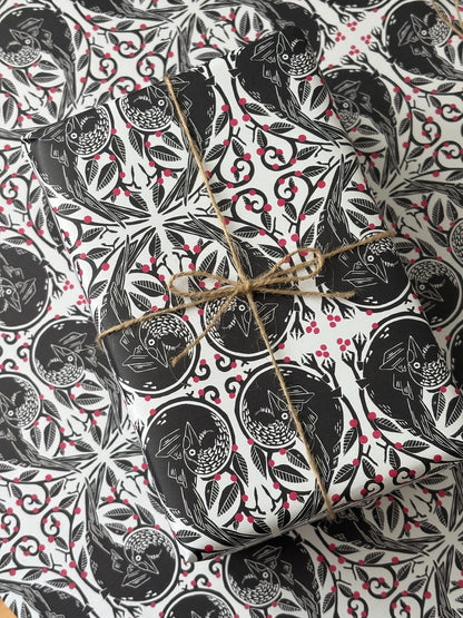 A gift box wrapped in black and white owl-patterned paper with red berries, tied with natural twine, photographed from above on a matching patterned surface.