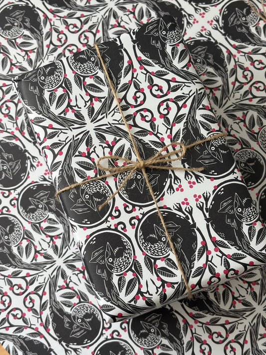 A gift box wrapped in black and white owl-patterned paper with red berries, tied with natural twine, photographed from above on a matching patterned surface.