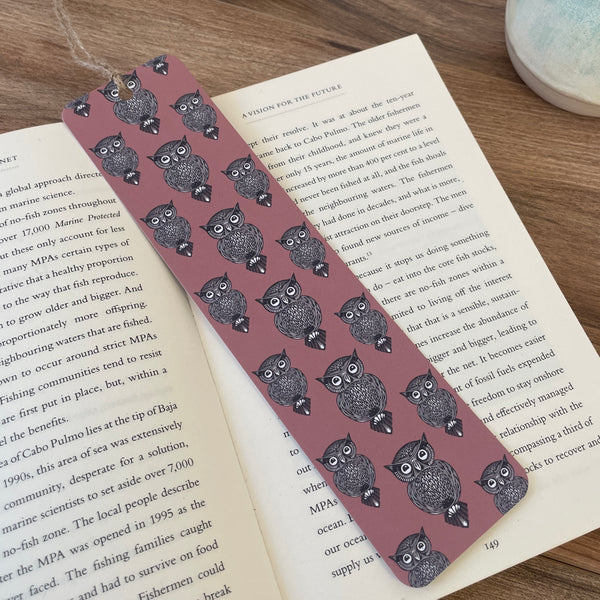 Repeat pattern Owl design on dusky pink background bookmark- features linocut design print. Bookmark resting across a paperback book with plant pot in background