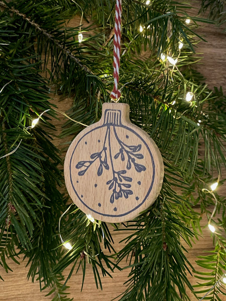 Video of wooden Christmas tree decoration spinning. Features navy linocut design of bauble hand printed on to beech wood paired with red and white twine