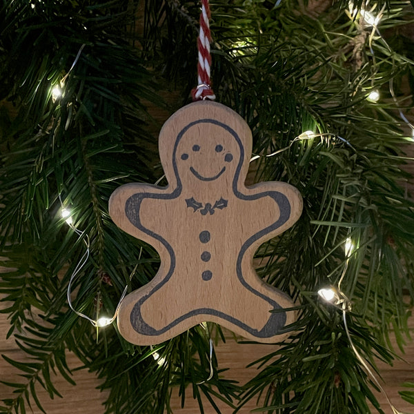 Video of wooden Christmas tree decoration spinning. Features navy linocut design of gingerbread man with holly bow tie hand printed on to beech wood paired with red and white twine