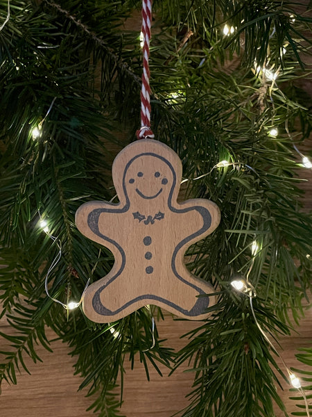 Video of wooden Christmas tree decoration spinning. Features navy linocut design of gingerbread man with holly bow tie hand printed on to beech wood paired with red and white twine