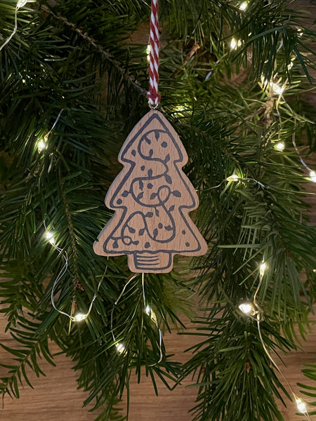 Video of wooden Christmas tree decoration spinning. Features navy linocut design of Christmas tree hand printed on to beech wood paired with red and white twine