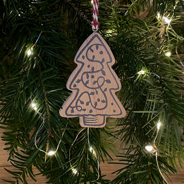 Video of wooden Christmas tree decoration spinning. Features navy linocut design of Christmas tree hand printed on to beech wood paired with red and white twine